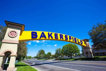 The image shows the Bakersfield sign, spanning over a street with a clear blue sky as the backdrop.