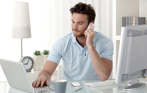 A guy using his laptop while talking to someone on the phone