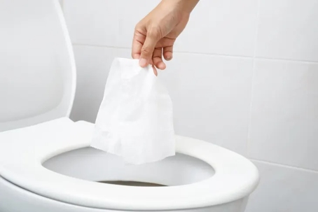 A hand is shown dropping a white tissue into a toilet bowl.