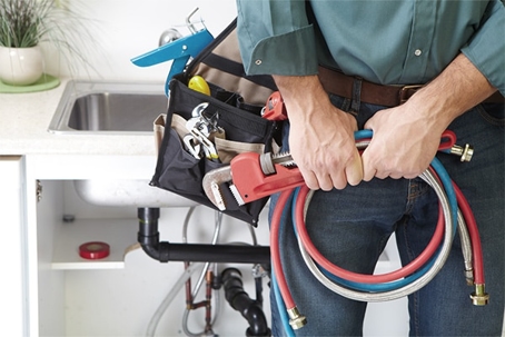 Plumber with tools and hoses at a kitchen sink.